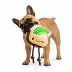 Un perro bulldog francés de color marrón claro de pie, sosteniendo el juguete de peluche Verný con forma de tostada y aguacate en su boca.
