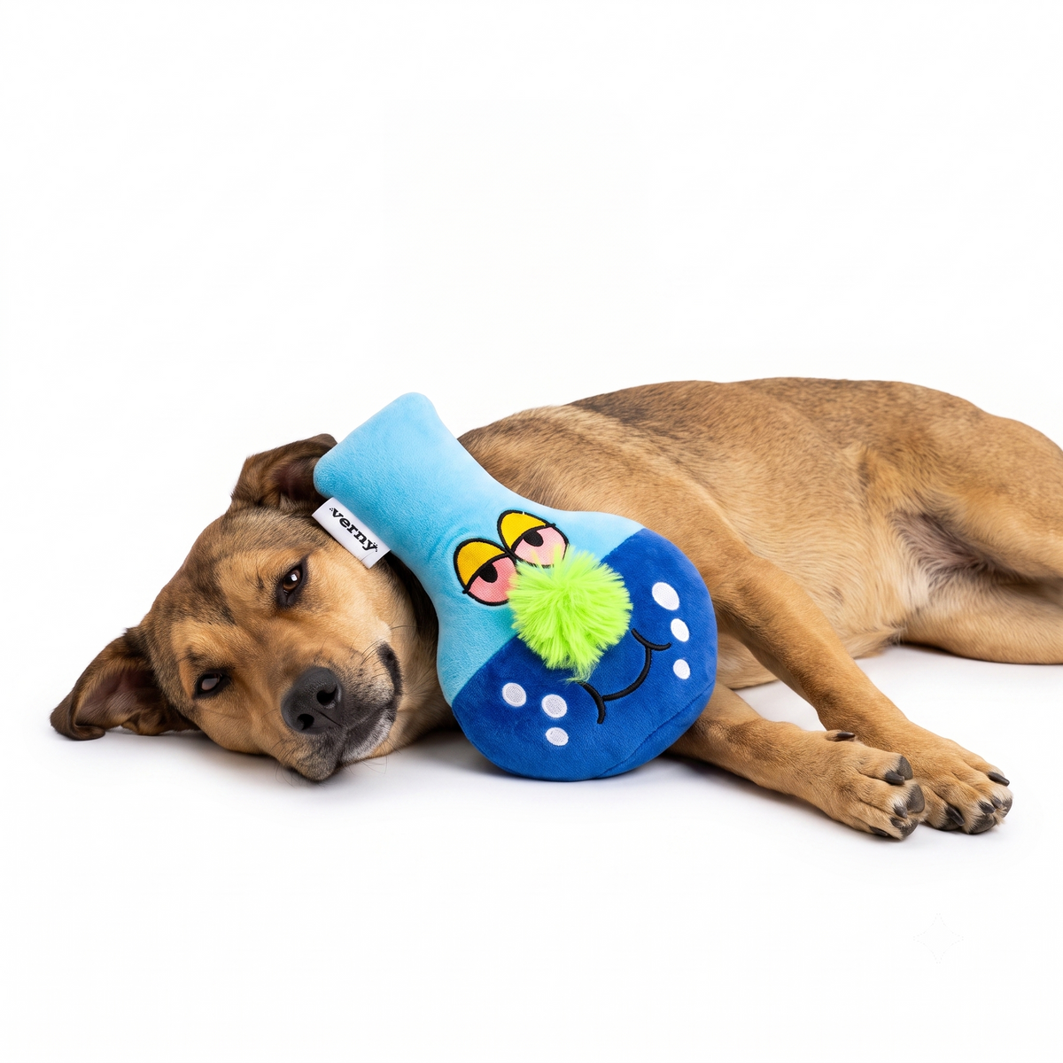 Un perro de pelaje marrón acostado en el suelo, descansando la cabeza cómodamente junto al juguete de peluche azul Verný